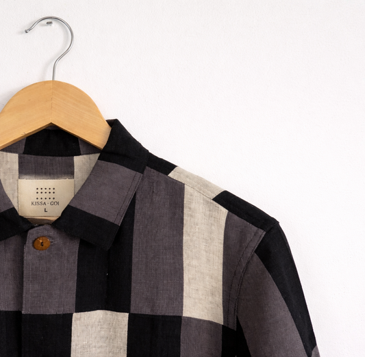 Closeup of patchwork checkered linen shirt with grey, white and black pattern displayed against a wall