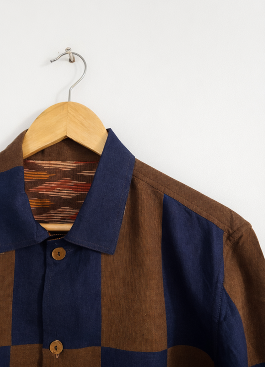Close up of patchwork checkered linen shirt with blue and brown pattern and ikkat lining displayed against a wall