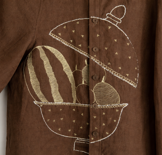 Detailed close up of brown jacket with fruit basket embroidered mukaish design displayed against a wall