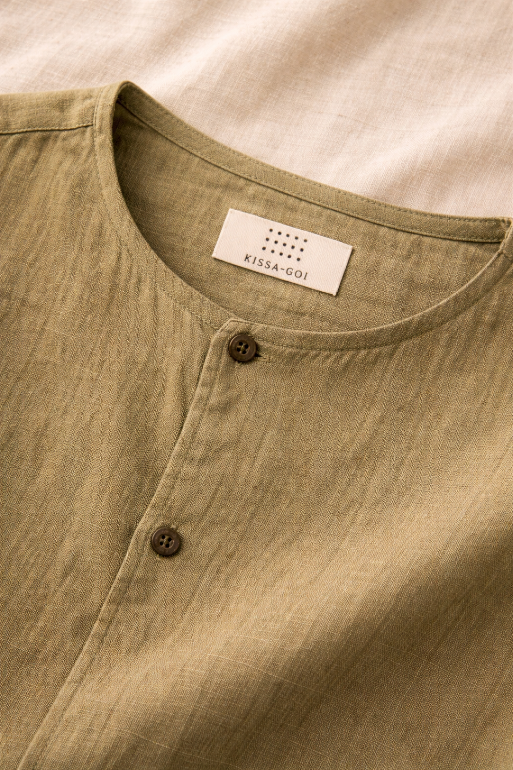 close up of Mustard Green Collarless Linen shirt displayed against a white fabric
