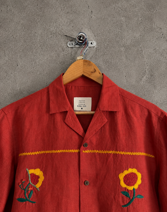 Embroidery details of Red shirt with floral embroidery on a wooden hanger against a gray wall.