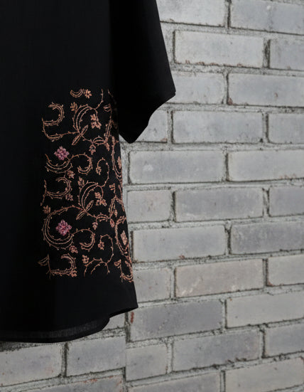 Close up detail of floral embroidery on black pashmina tshirt displayed against grey brick wall