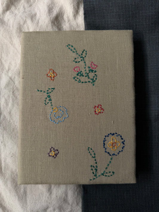 Hand-embroidered flowers on the cover of white diary displayed against dark and white background