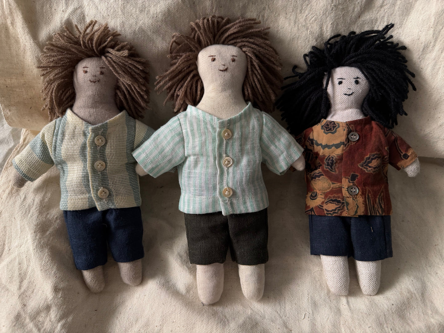 Three first friend hand-stitched dolls place together and displayed against a white fabric