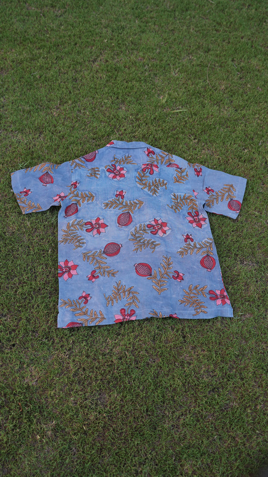 Flatlay of a blue hand-painted linen shirt with pomegranate vines and leaves