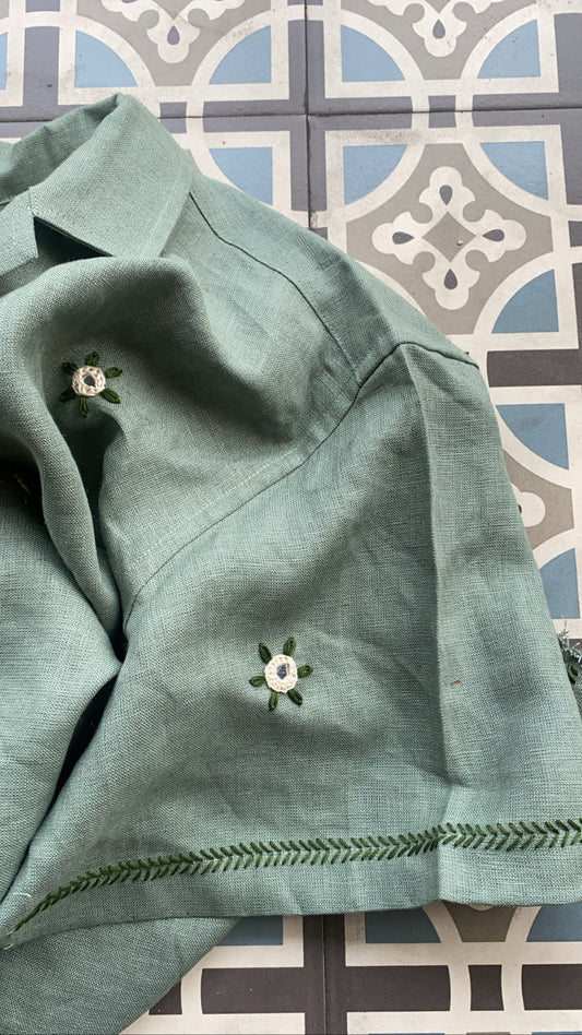 Details of a green linen shirt with flowers embroidered throughout. The flowers have mirror in its centre