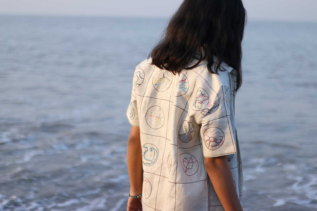 Back of a girl in a beige half-sleeved linen shirt with Hand-embroidered circular maps of cities