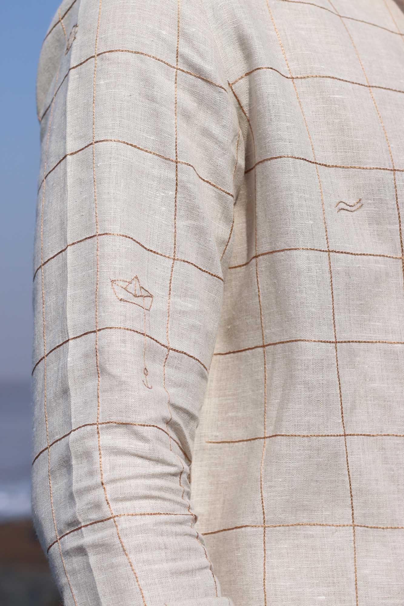 Sleeve details of a beige linen shirt with small embroidered checks and beach elemets like boats, fish shells interspersed throughout