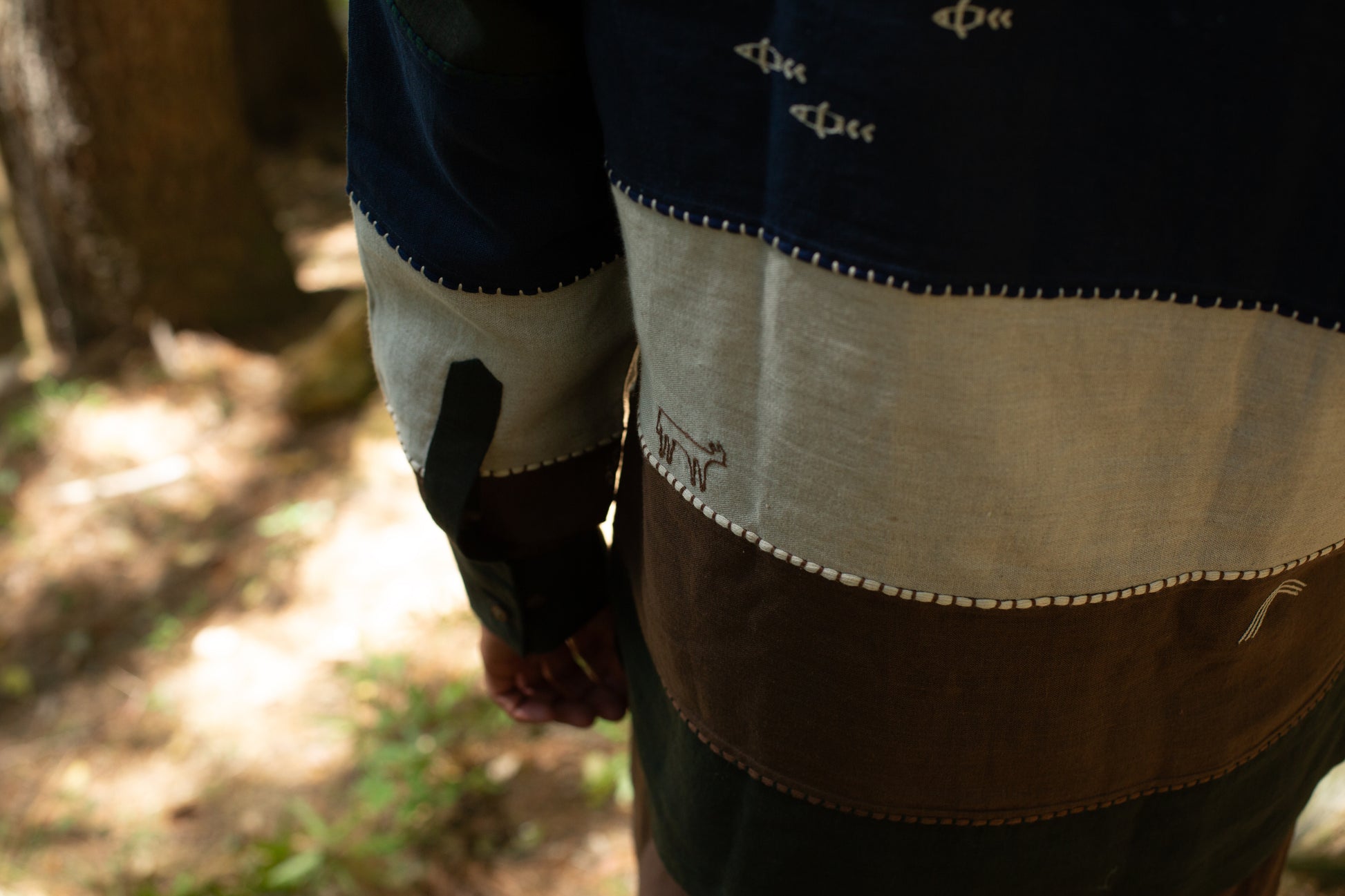 Model wearing a panelled linen shirt with goat and fish embroidery in a natural setting
