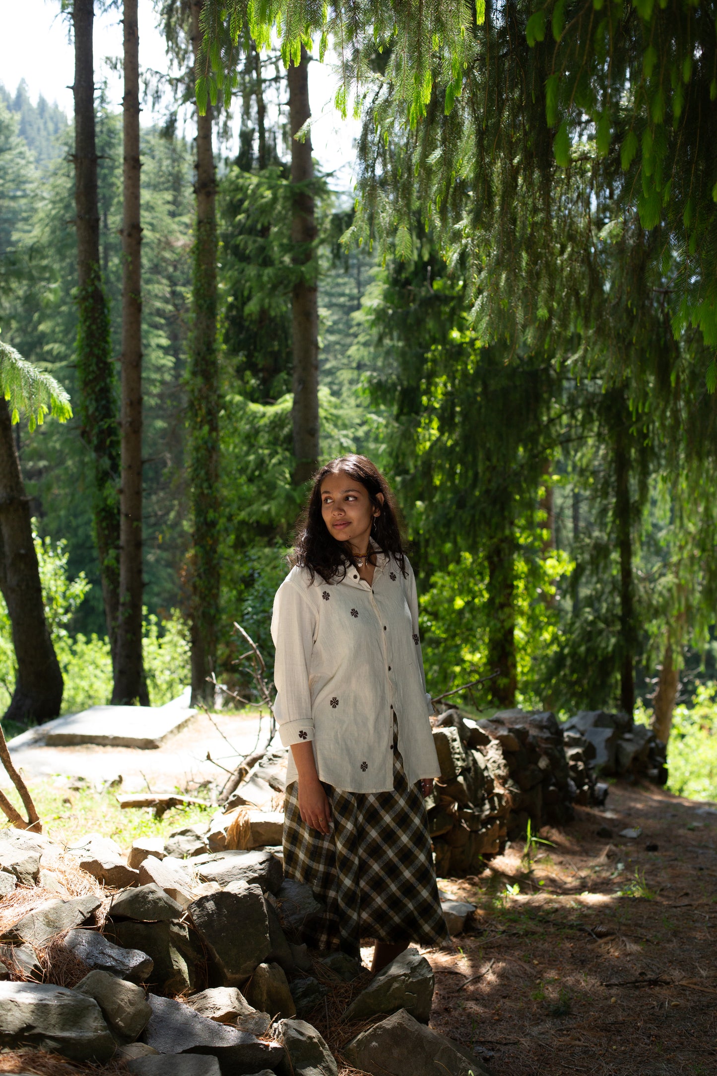 Woman wearing a cotton shirt with traditional suf embroidery standing in a forest with trees and rocks around