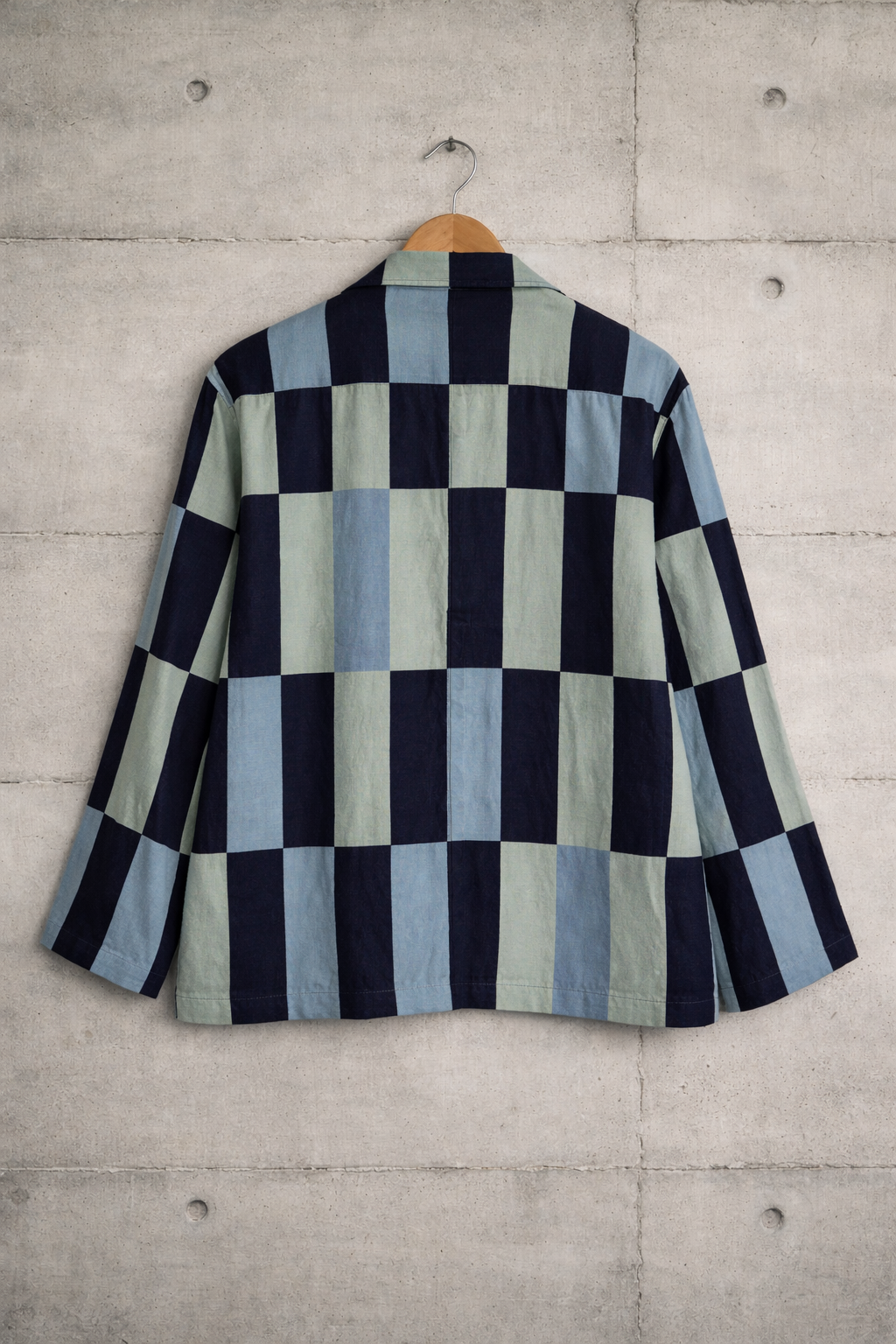 Back of patchwork checkered linen shirt with dark blue, light green, and light blue pattern displayed against a wall