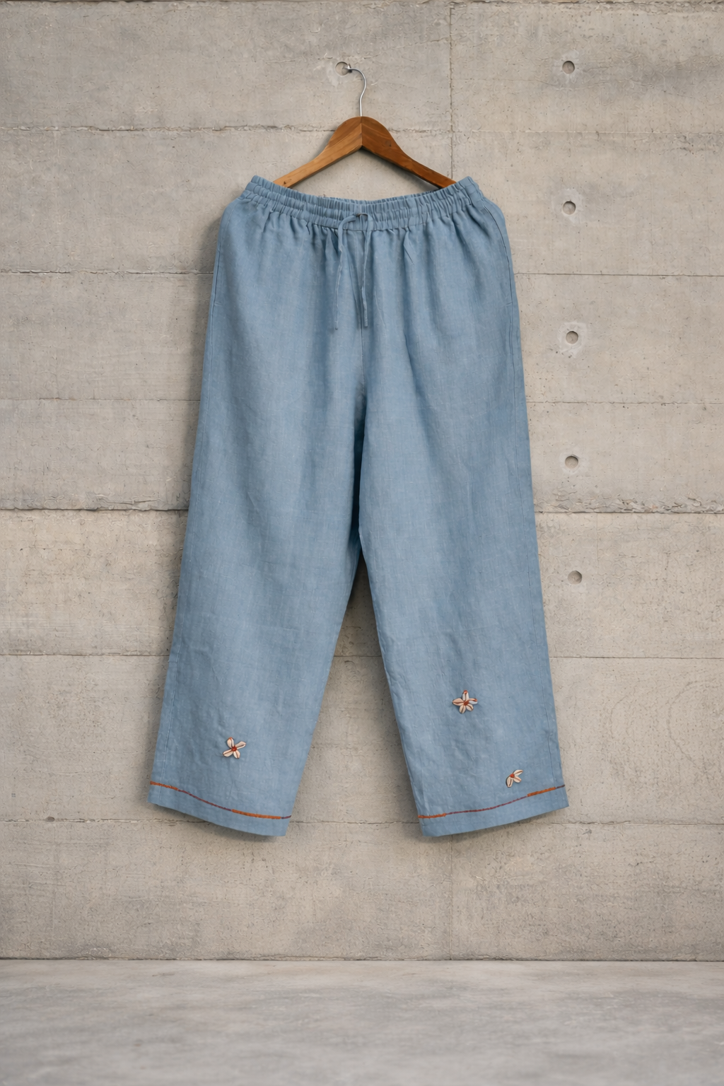Light blue Cowrie flowers lounge embroidered linen pants against a wall