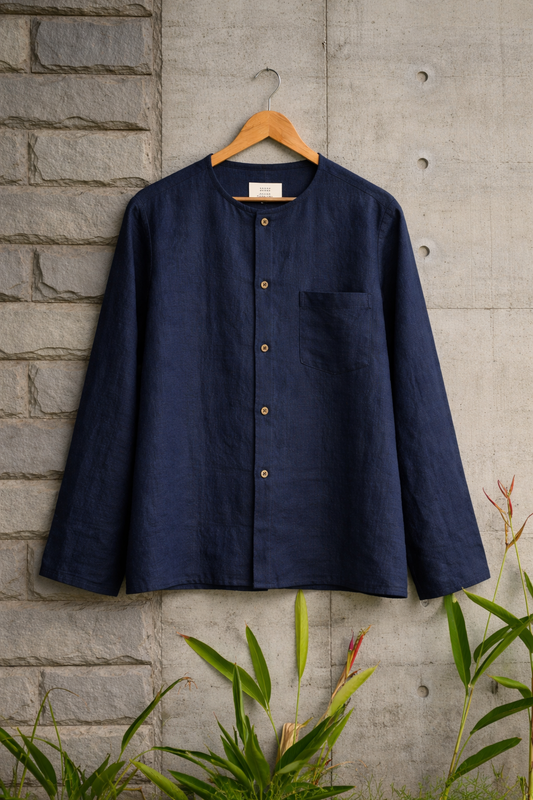 Blue collarless linen shirt displayed against a grey wall
