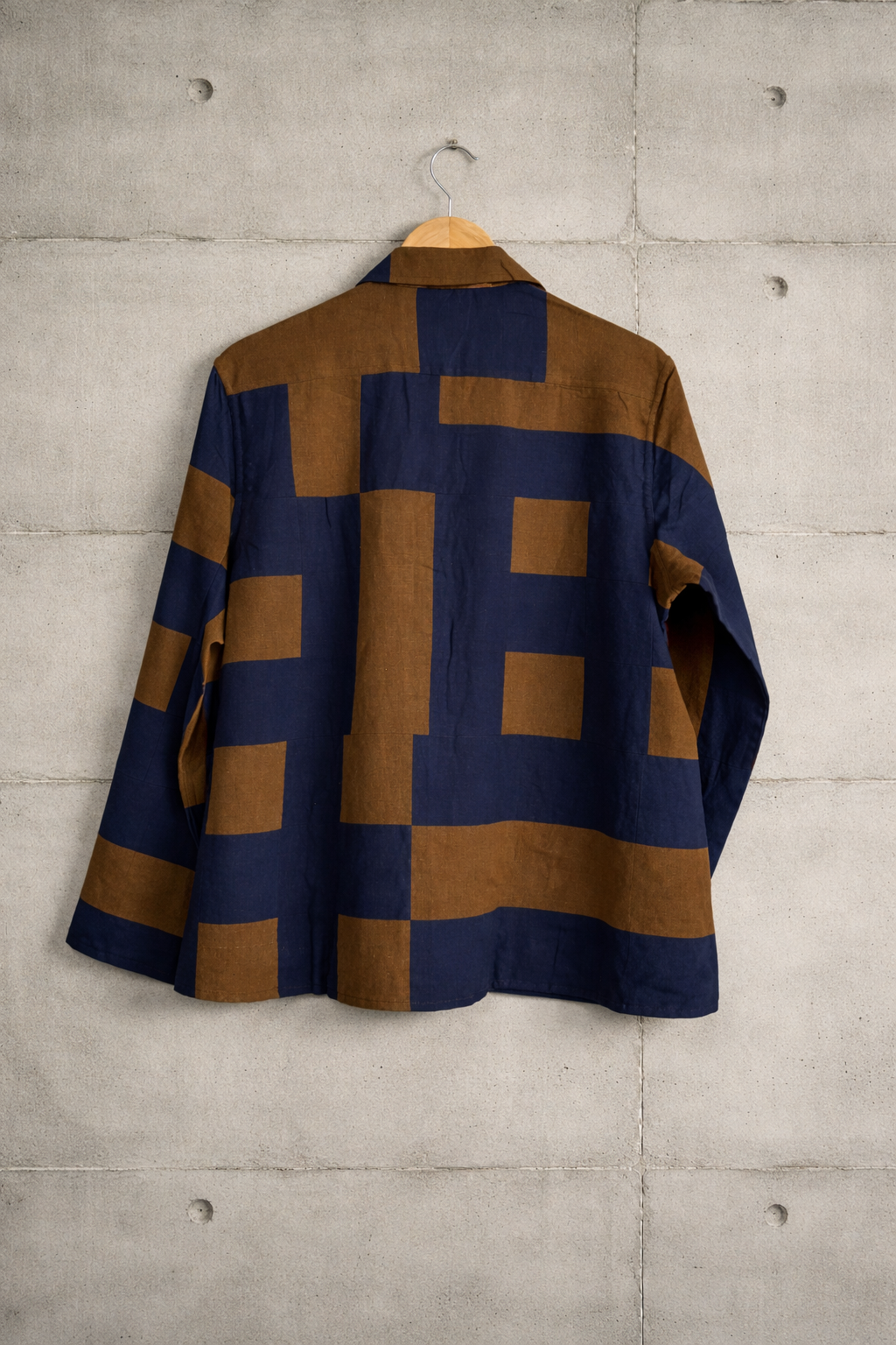 Back of patchwork checkered linen shirt with blue and brown pattern displayed against a wall