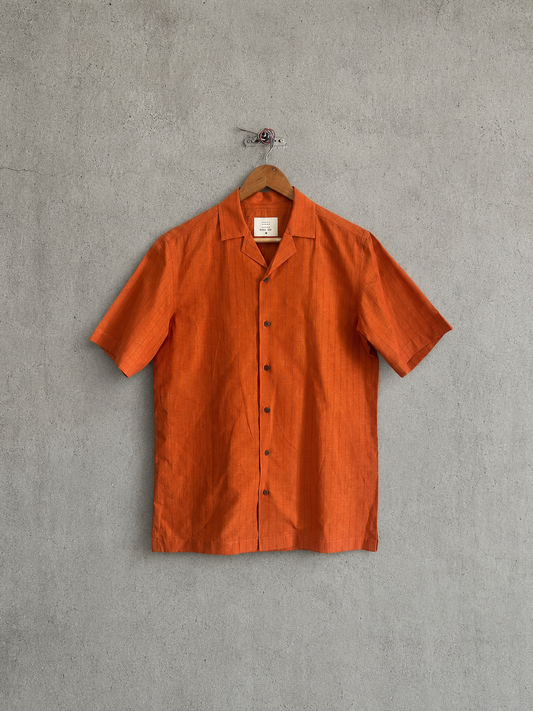 Orange short-sleeve shirt on a wooden hanger against a gray concrete wall.