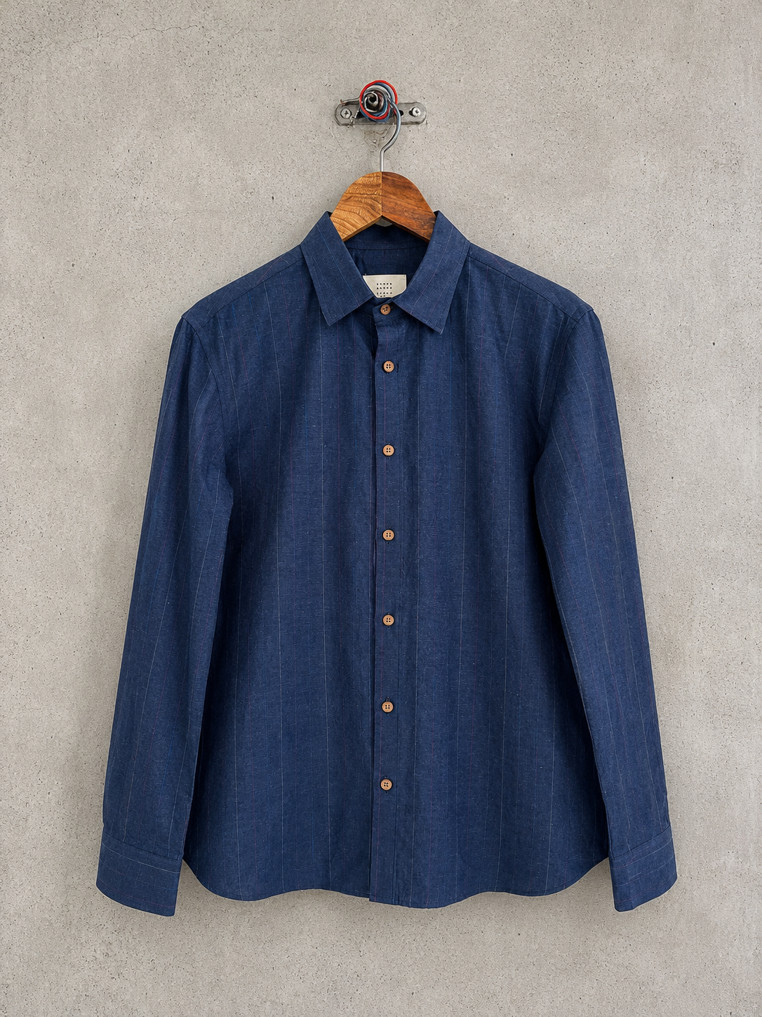 Blue shirt on a wooden hanger against a concrete wall