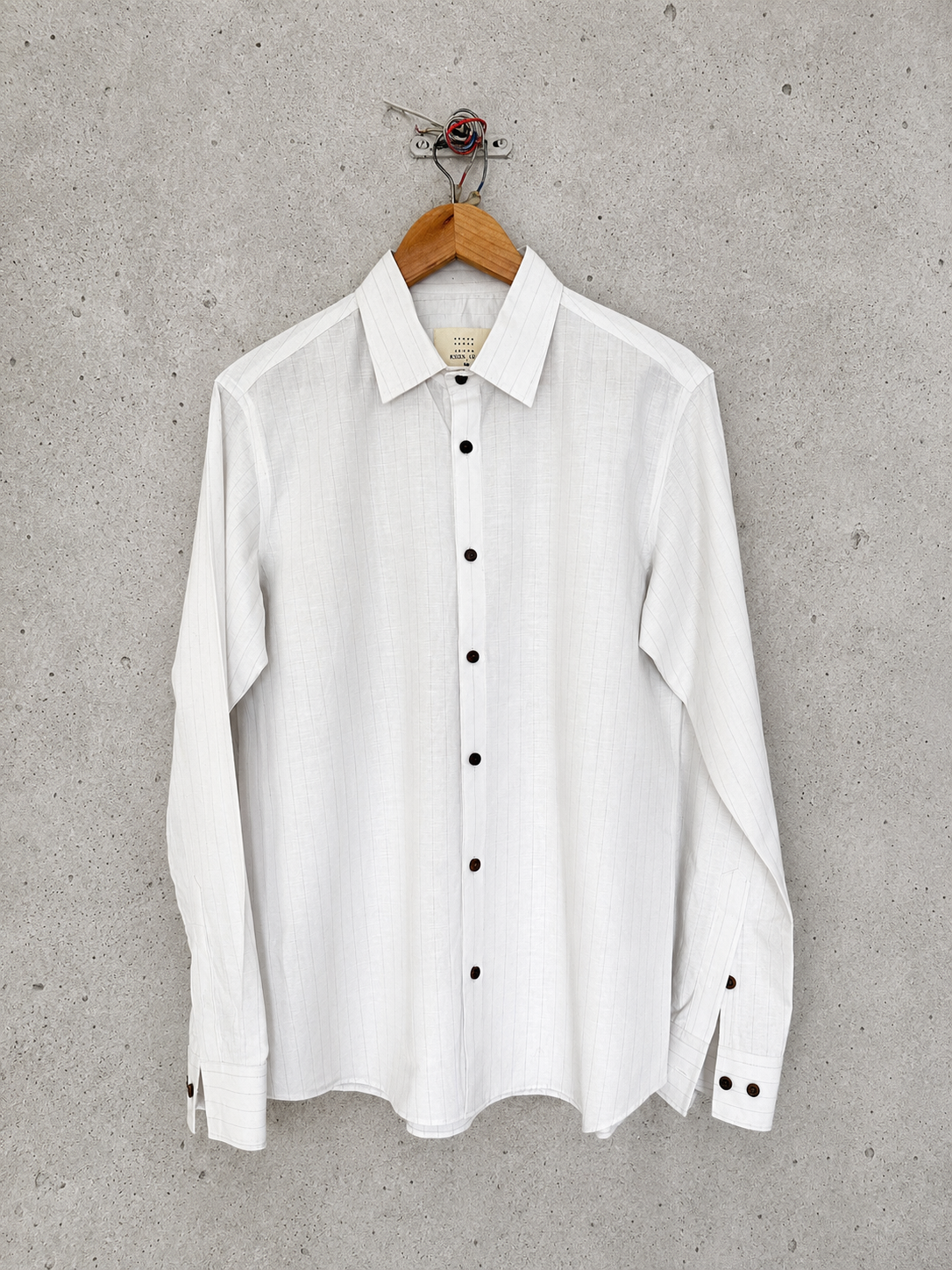 White striped shirt with black buttons on a hanger against a gray concrete wall