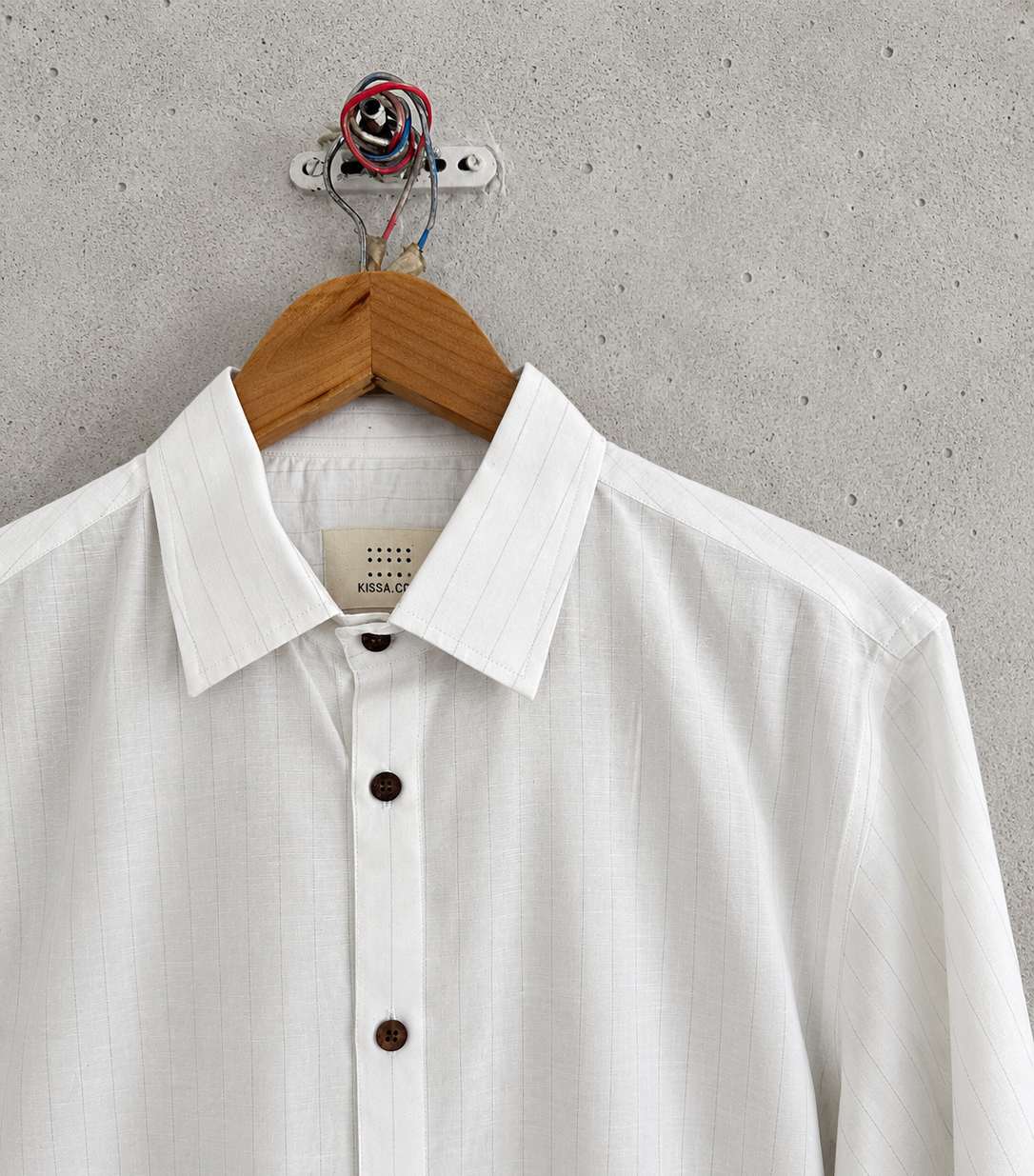 White striped shirt with brown buttons on a wooden hanger against a gray concrete wall.