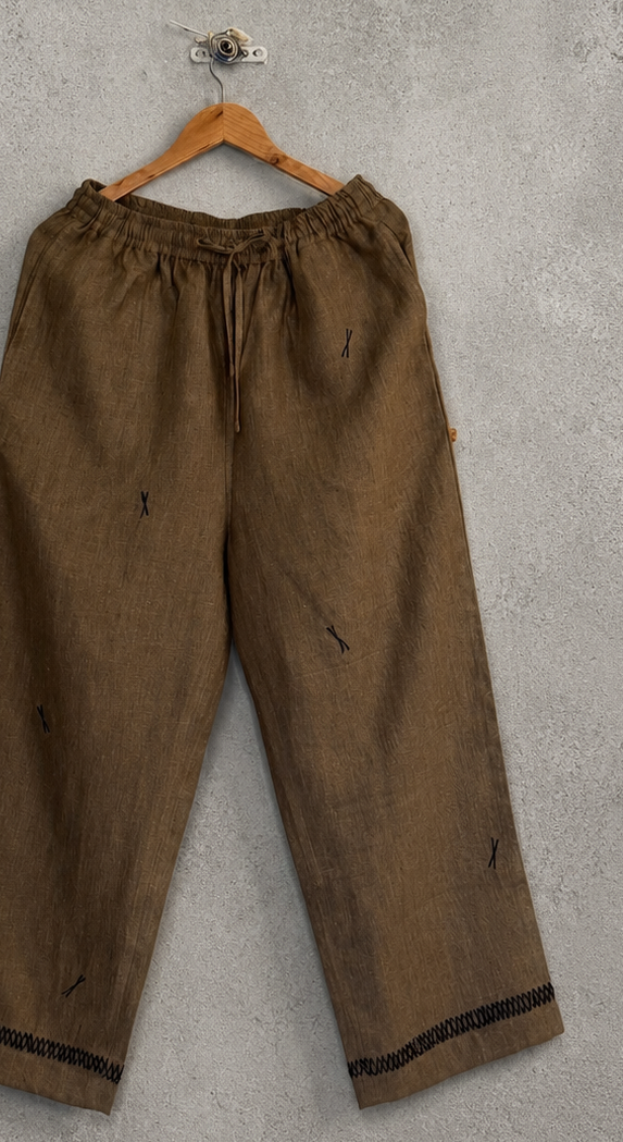 Zoomed in brown pants on a hanger against a gray concrete wall