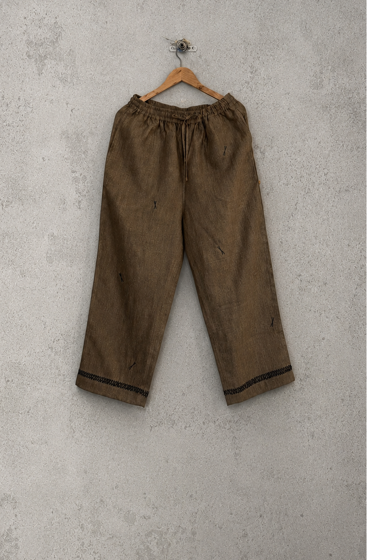 Brown pants hanging on a wooden hanger against a gray concrete wall.