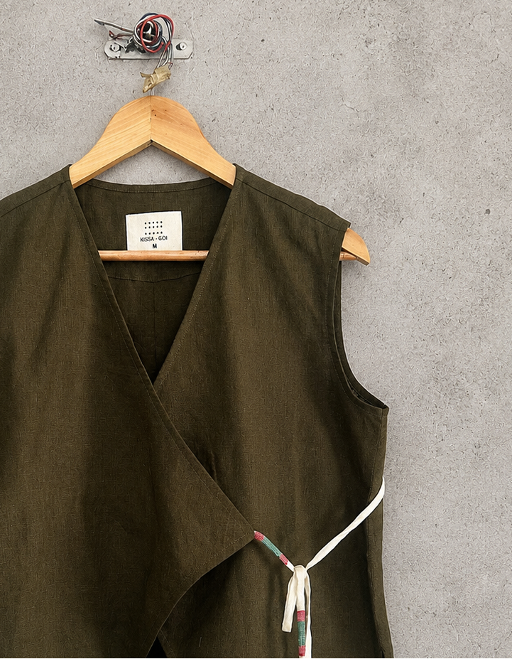 Green vest with a tie on a wooden hanger against a gray concrete wall