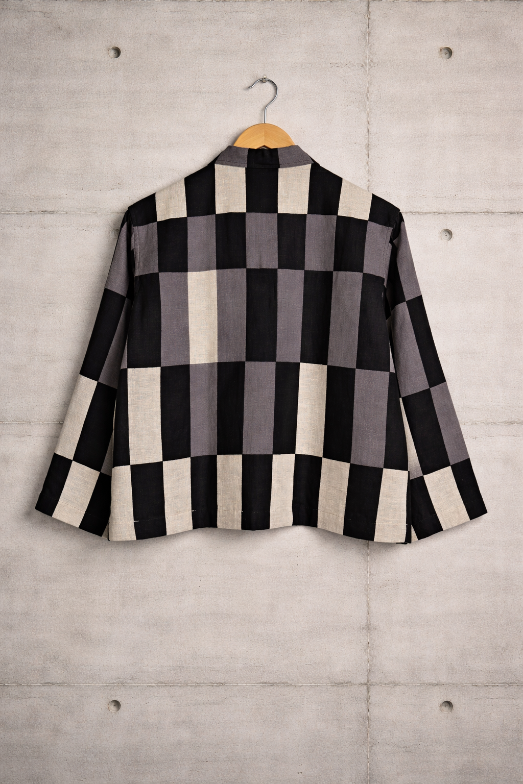 Back of patchwork checkered linen shirt with grey, white and black pattern displayed against a wall