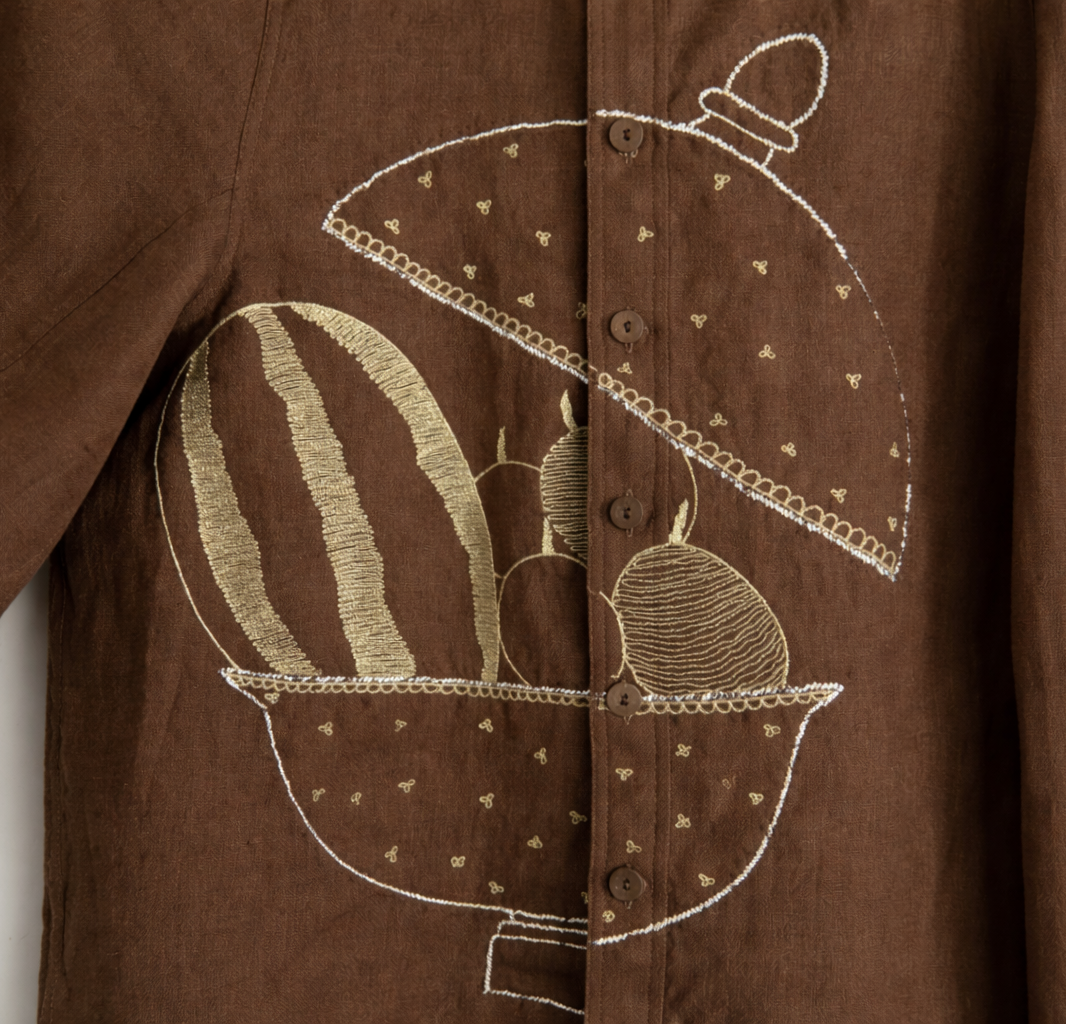 Detailed close up of brown jacket with fruit basket embroidered mukaish design displayed against a wall