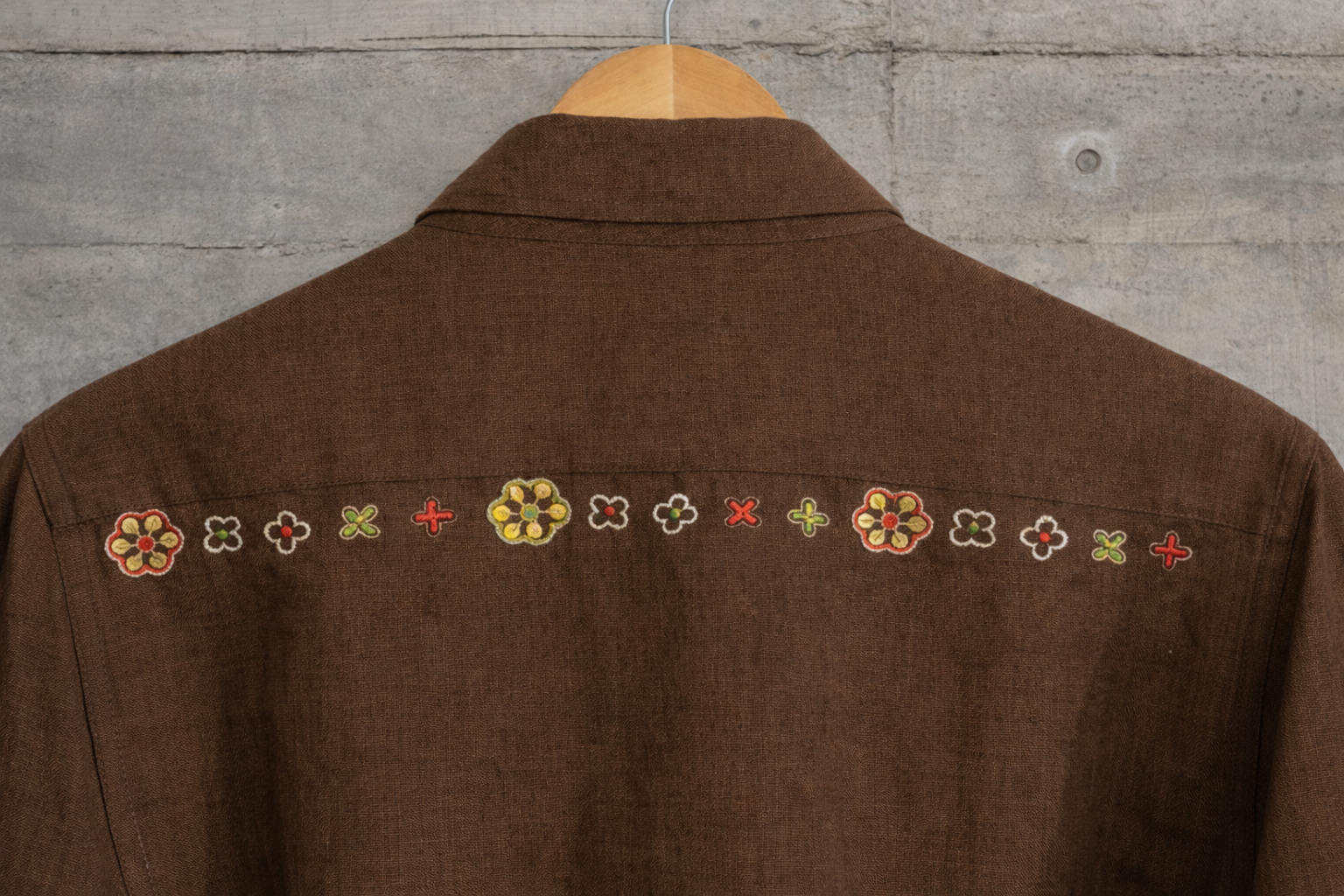 Back details of brown jacket with zari flower motif displayed against a wall.