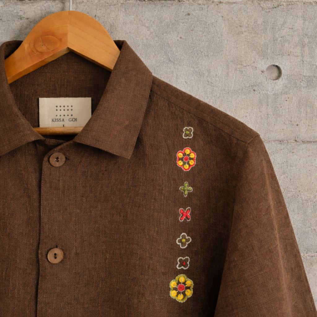 Close up of brown jacket with zari flower motif displayed against the wall.