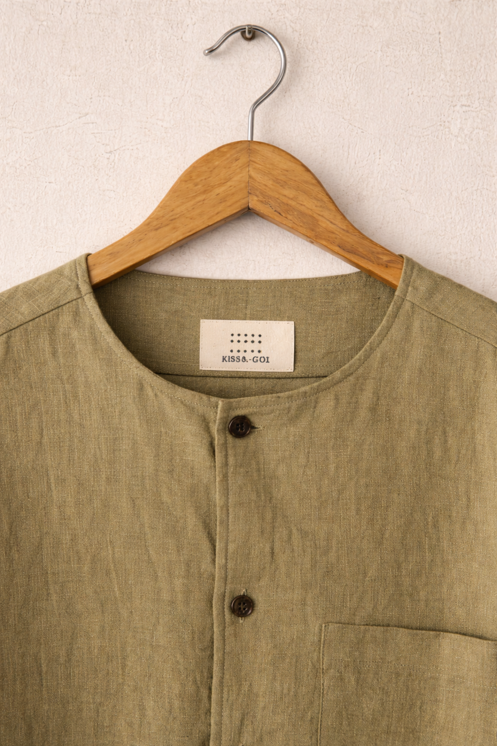 close up of Mustard Green Collarless Linen shirt displayed against a grey wall