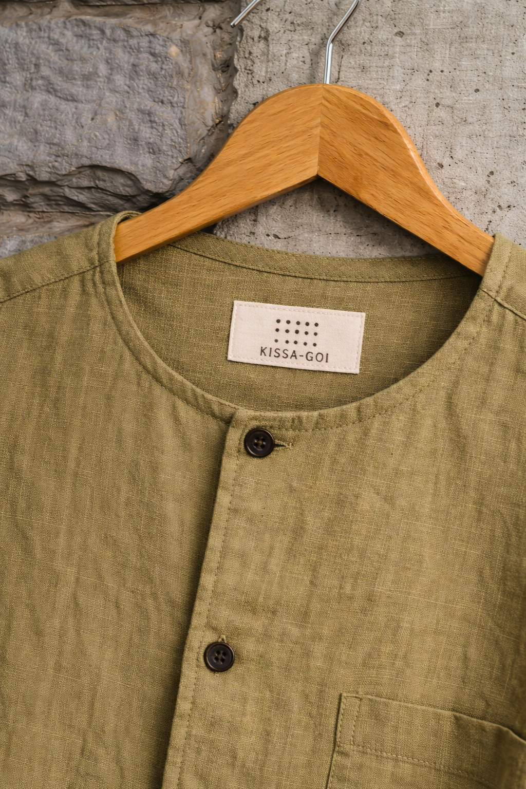 close up of Mustard Green Collarless Linen shirt displayed against a grey wall