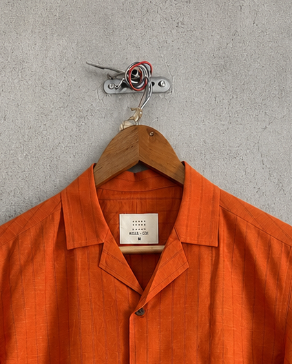 Orange short-sleeve shirt on a hanger against a gray concrete wall