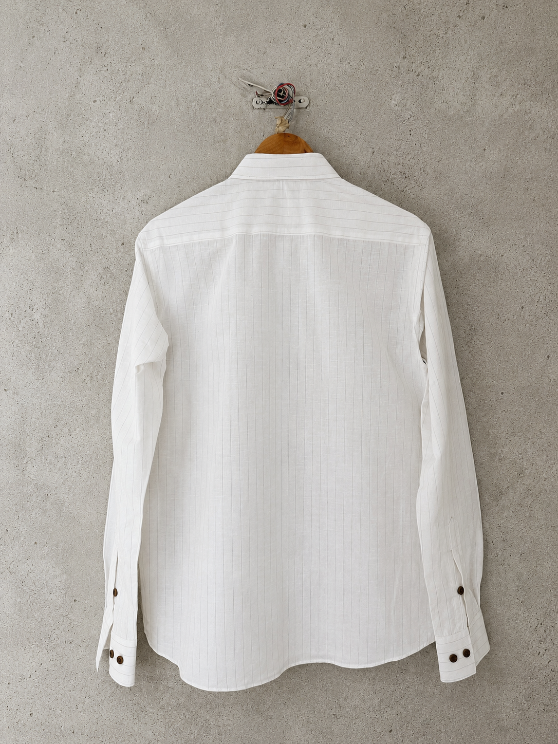 Back of a white striped shirt on a wooden hanger against a gray concrete wall