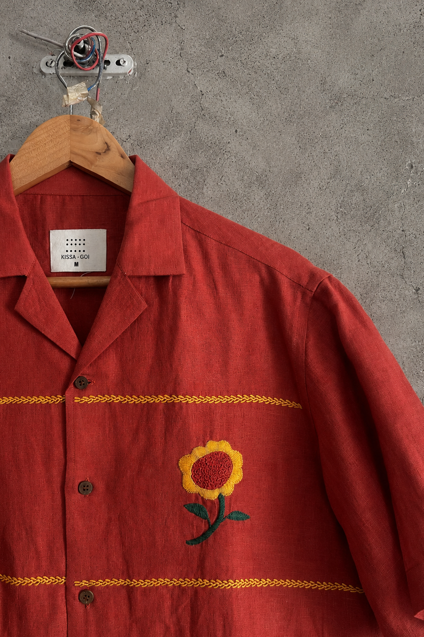 Zoomed in Red shirt with floral embroidery on a hanger against a gray wall