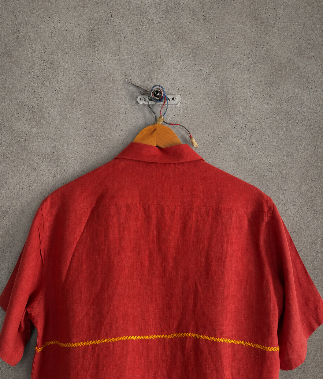 Back of a red shirt on a hanger against a gray wall
