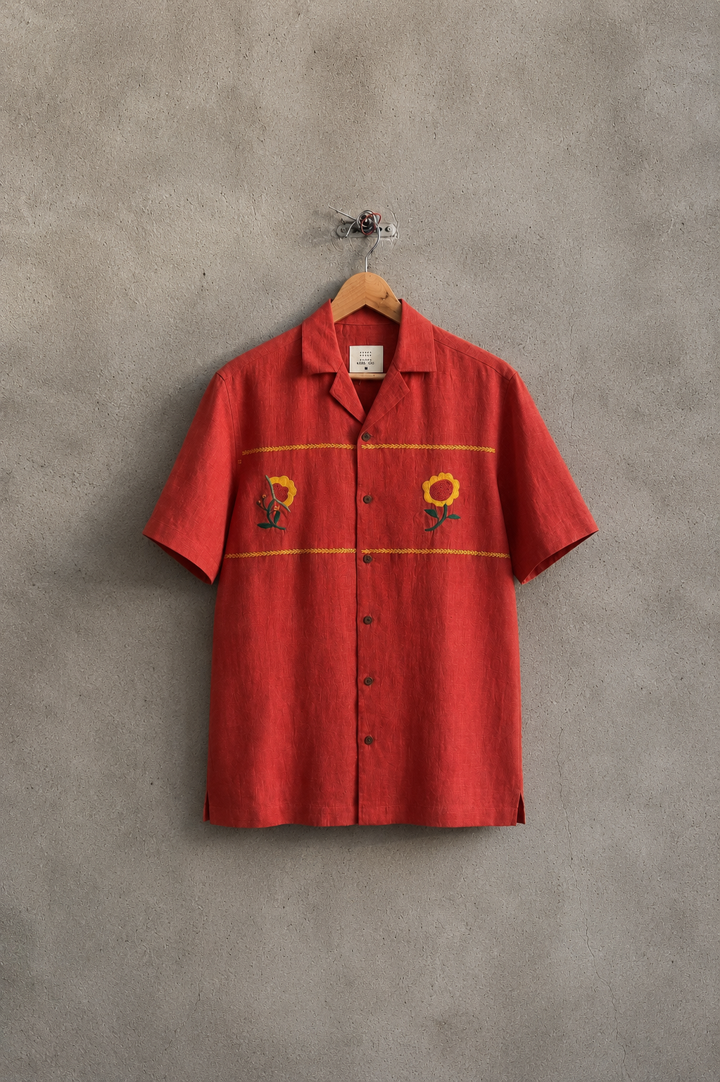 Red shirt with floral patterns on a hanger against a gray concrete wall