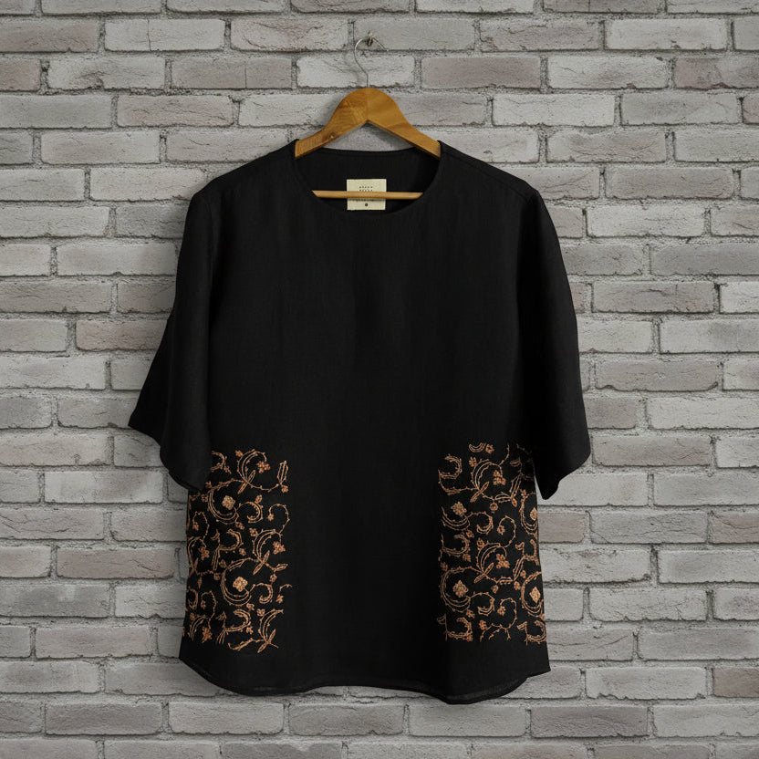 Floral embroidery on black pashmina tshirt displayed against grey brick wall 