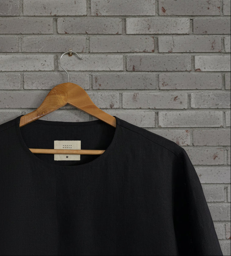 Black pashmina tshirt closeup displayed against grey brick wall 