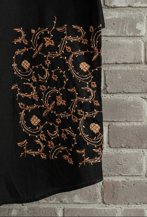 Close up detail of floral embroidery on black pashmina tshirt displayed against grey brick wall 