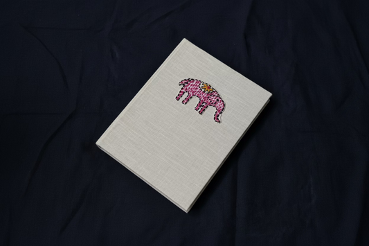 White diary with a pink elephant embroidered on it placed against a dark background.