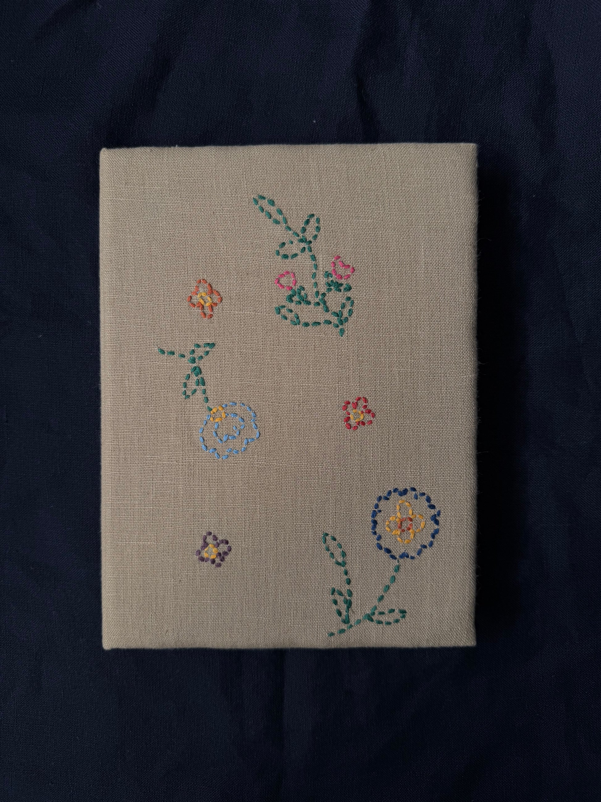 Hand-embroidered flowers on the cover of white diary displayed against dark background