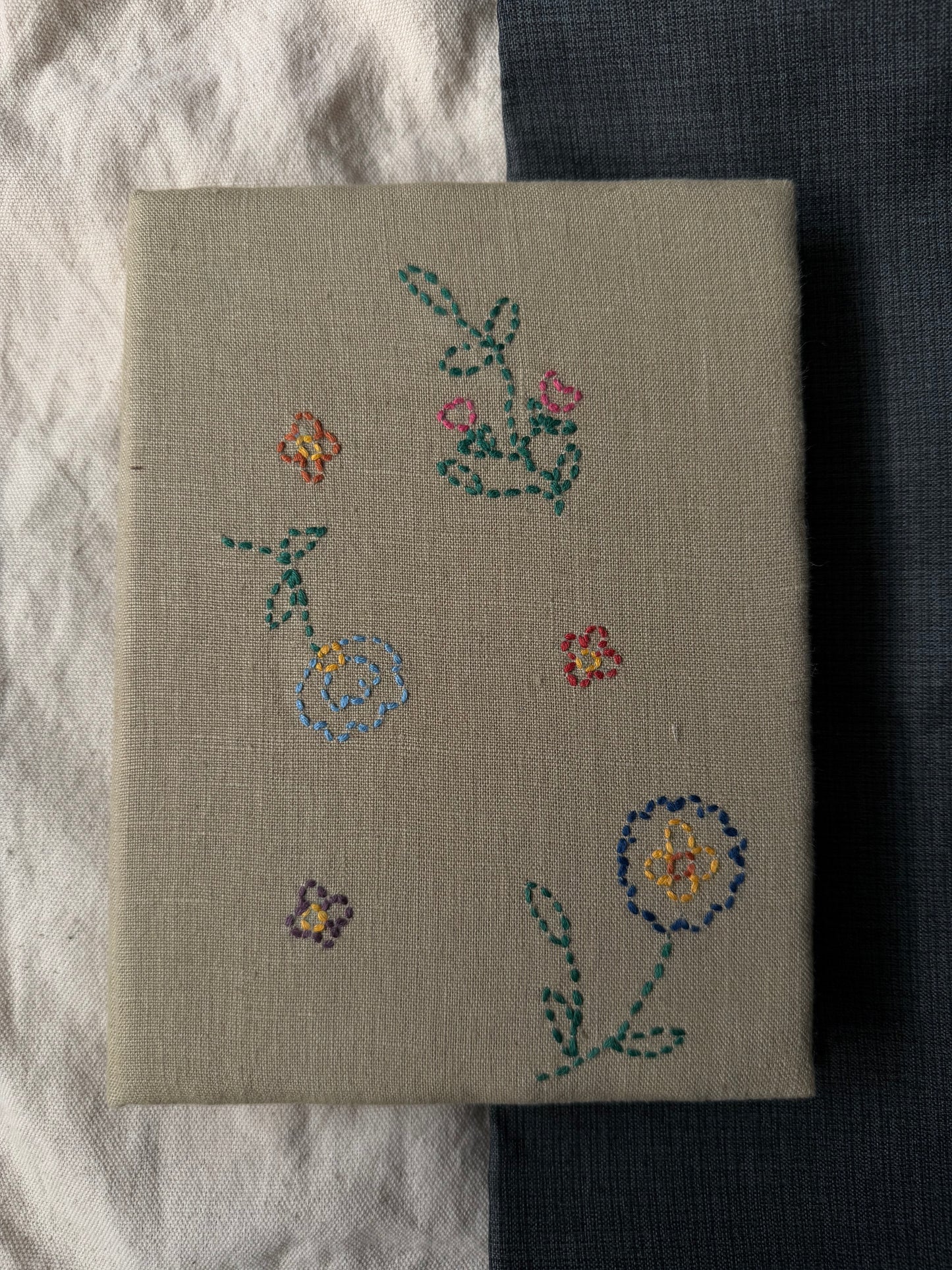 Hand-embroidered flowers on the cover of white diary displayed against dark and white background
