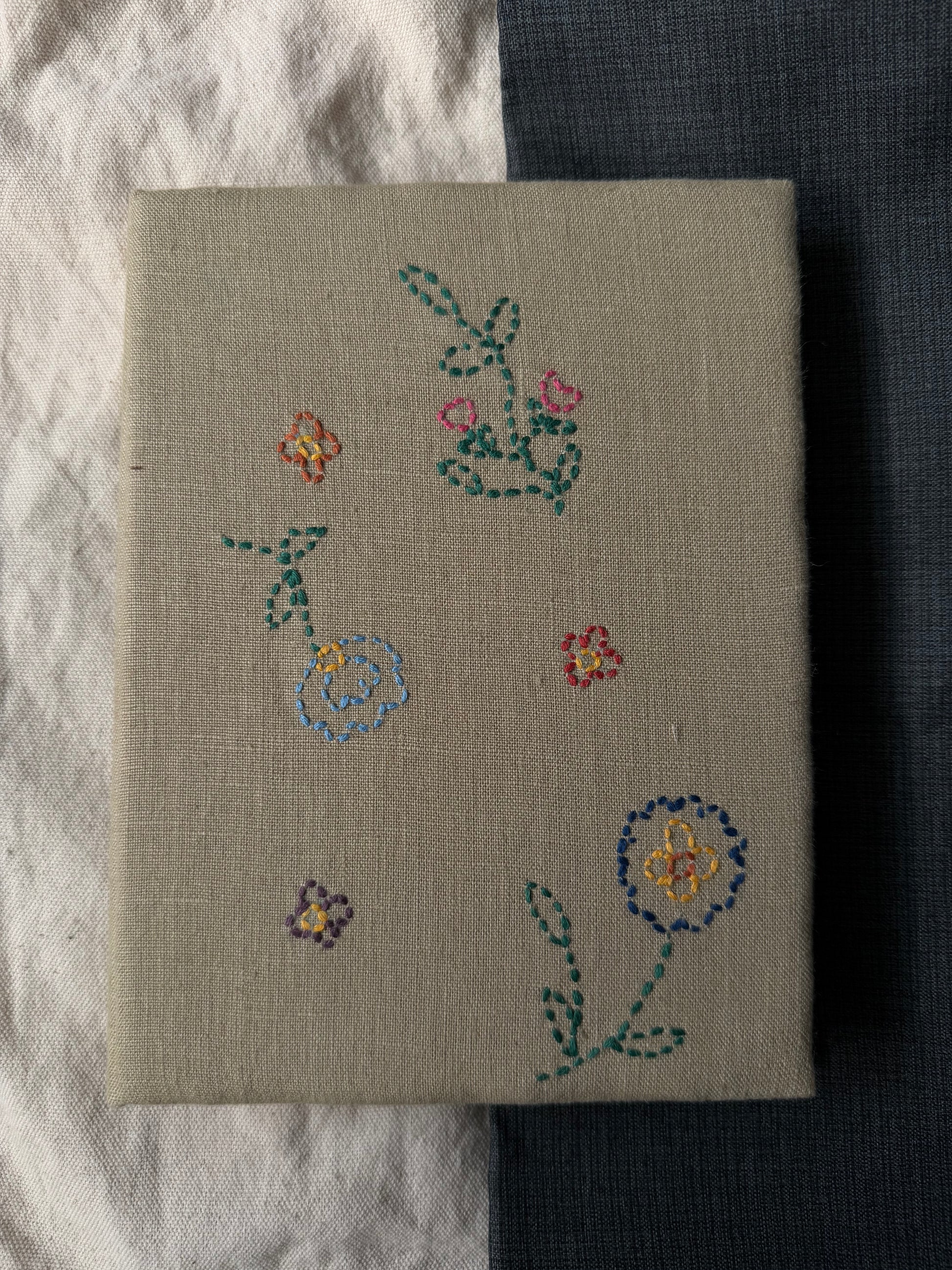 Hand-embroidered flowers on the cover of white diary displayed against dark and white background