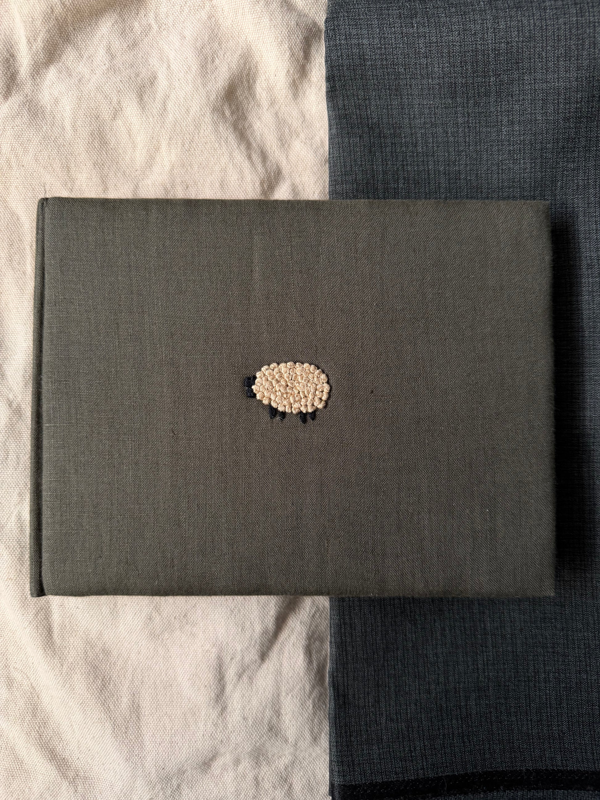 Olive green sheep sketchbook displayed against white and dark  background.