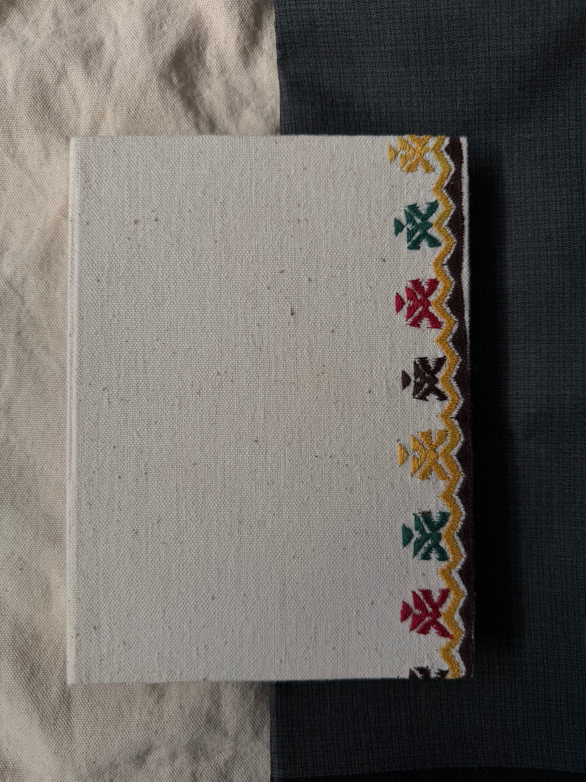 Along the Edge suf embroidered diary placed against a contrasting white and dark surface