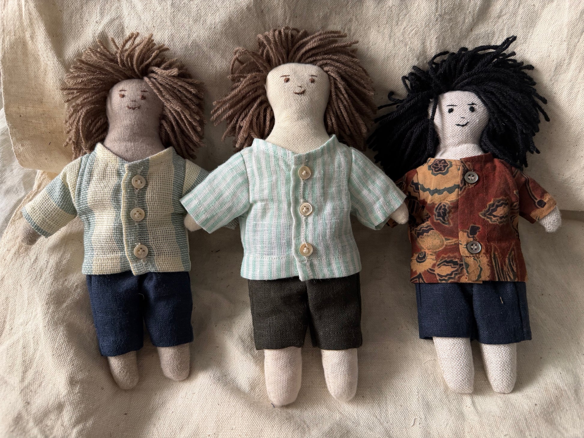 Three first friend hand-stitched dolls place together and displayed against a white fabric